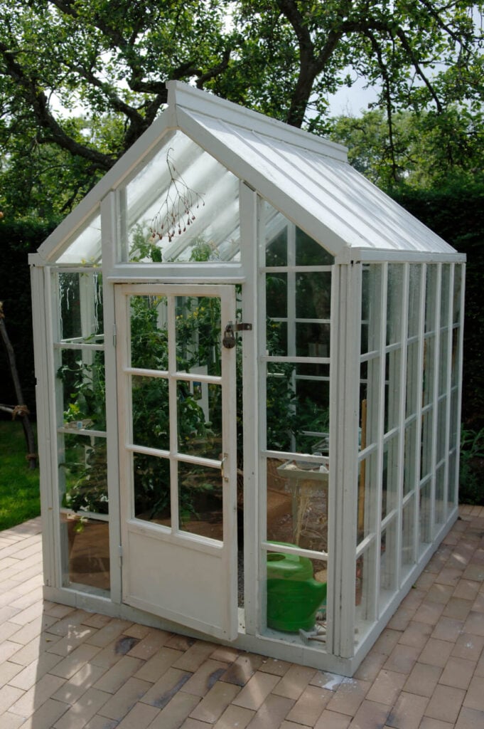 一个白色的小温室兼作园艺棚。这个结构被放置在砖砌的露台上。
