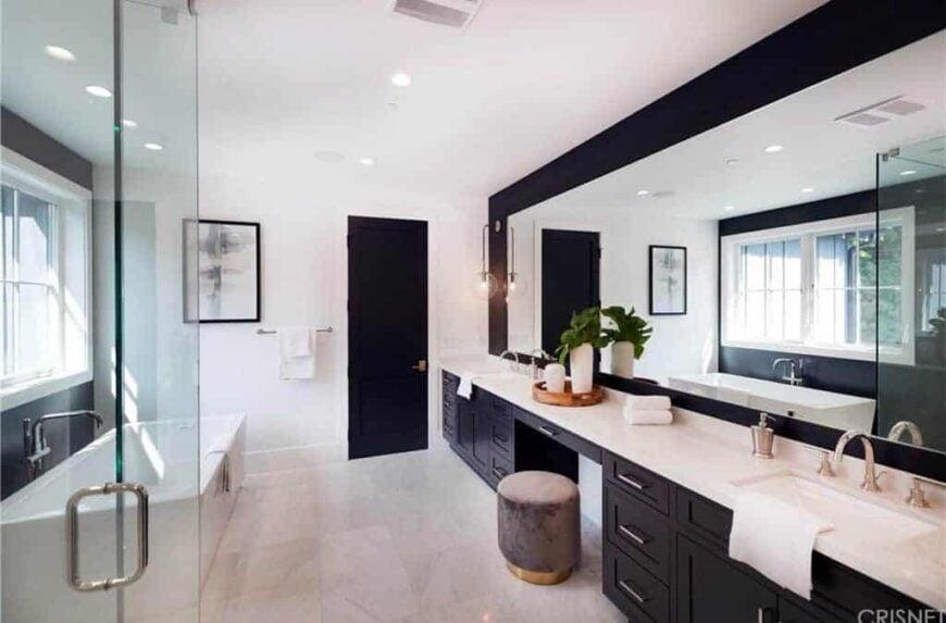 这是一个与上一个风格非常不同的浴室，但你很快就会注意到，在这个系列中没有两个浴室是相同的，这表明你可以在一个有这么多标准要求的房间中获得多么有创意!这是一个非常简单和现代的浴室设计，黑色的橱柜和白色的大理石台面形成了可爱的对比。美丽的轻石瓷砖保持配色方案，与墙壁和门上不寻常的黑色油漆形成对比。这可不是每天都能看到的!在一个巨大的景观窗的对面放置一面景观镜是非常聪明的，因为它只会使进入房间的光线增加一倍，而且你也可以在准备的时候看到可爱的室外景色。我们不能忘记那个漂亮的浴缸!
