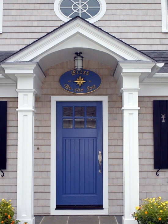 这座房子的外墙是米色的砖，有一个蓝色的前门，上面有一个白色的门廊。它由安装在桶形拱形天花板上的玻璃平视灯照明。