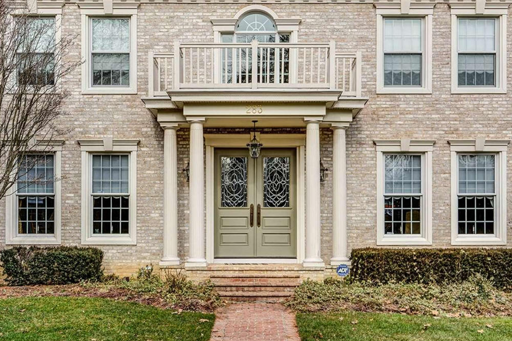这座砖房子提供了一个华丽的铅玻璃双门，周围是白色的柱子。它由锻铁吊坠和配套的烛台照明。