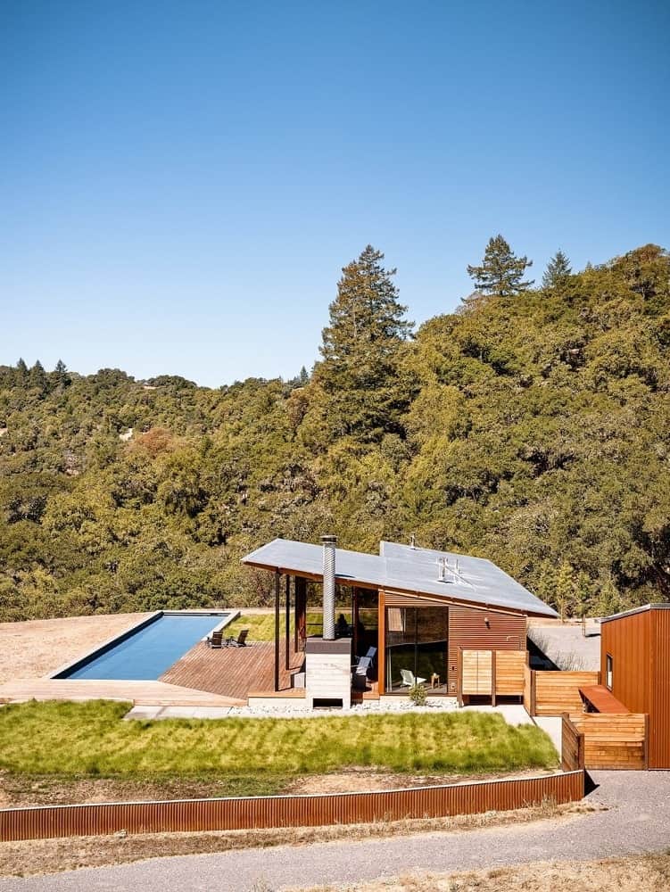 这个简单而迷人的房子有一个倾斜的屋顶，与外部的木板和玻璃墙相辅相成。这些玻璃窗和室外区域的设计是为了更好地欣赏周围的景观，以及后院美丽的游泳池和蓬松的草坪。