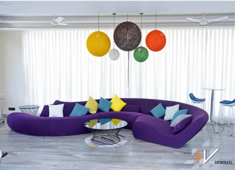 一个带有方形枕头的紫色s形沙发被放置在中心，而内部可以注意到彩色的大型圆形灯。