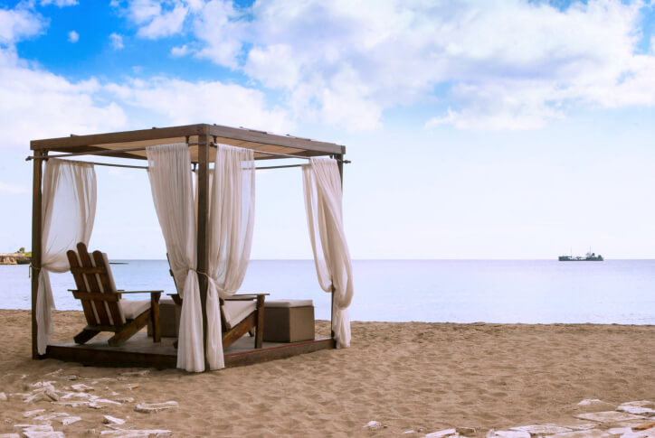 一个方形凉亭，配有透明窗帘和阿迪朗达克椅。凉亭眺望水面，拥抱海滩的美感。