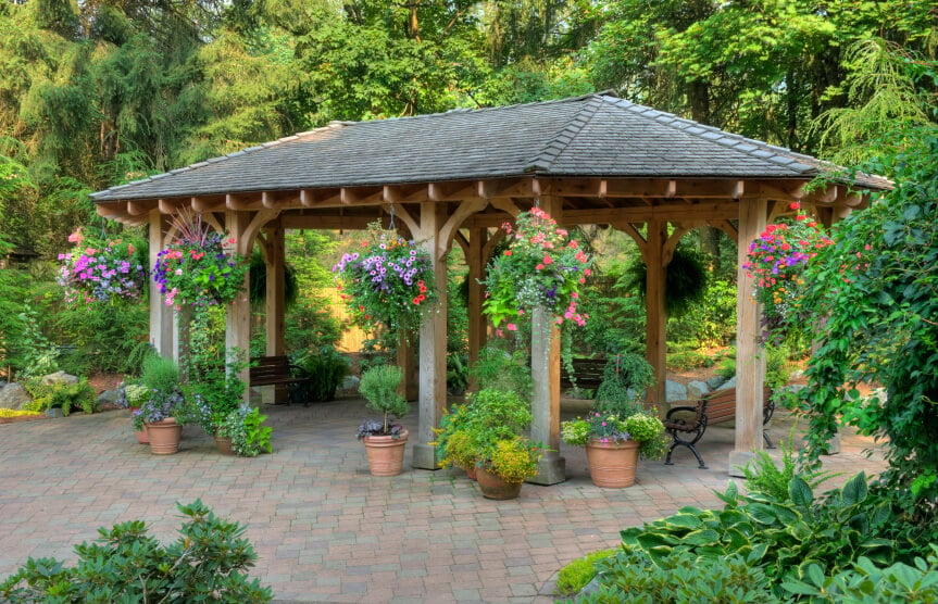 砖砌露台上的花园亭式凉亭。虽然周围的区域郁郁葱葱，但凉亭却与众不同。吊篮和集装箱花园有助于将庭院的两个部分整合在一起。
