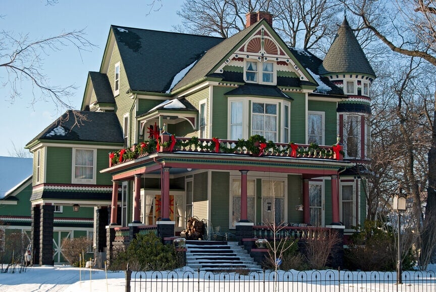大的绿色，黑色和红色的维多利亚式住宅与前廊和砖基础。
