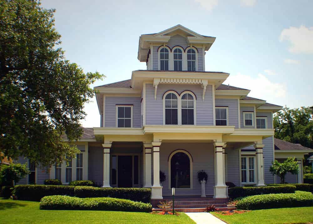 设计简单的紫色和白色维多利亚式住宅，有大前廊和拱形窗户。