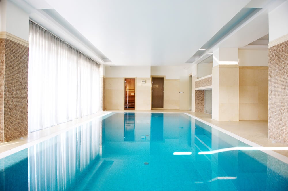 桃色和白色设计的室内泳池房，全墙的窗户提供充足的自然光线。