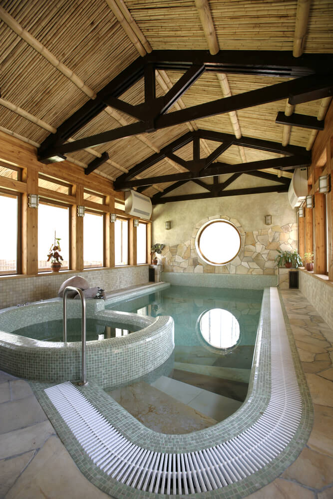 石头，瓷砖和木材室内游泳池和热水浴缸。天花板上裸露的木梁给它带来了更大的空间外观。房间四周都是窗户，自然光线充足。