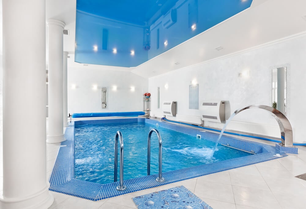 全白色的室内泳池，白色的柱子和蓝色的屋顶。泳池包括银色喷泉壶嘴在一个角落。