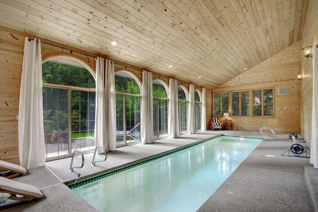 倾斜的木天花板室内在地面游泳池，一面墙与地板到天花板的拱形窗户。