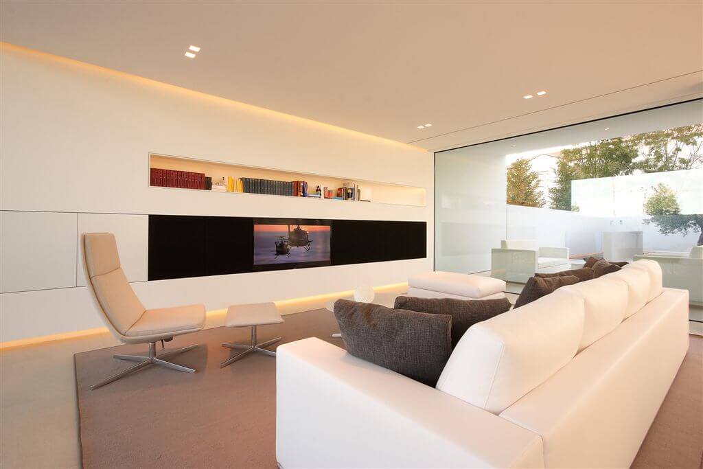 前面的客厅有浅棕色的地板和皮椅，全白的墙壁和黑色的迷彩电视。