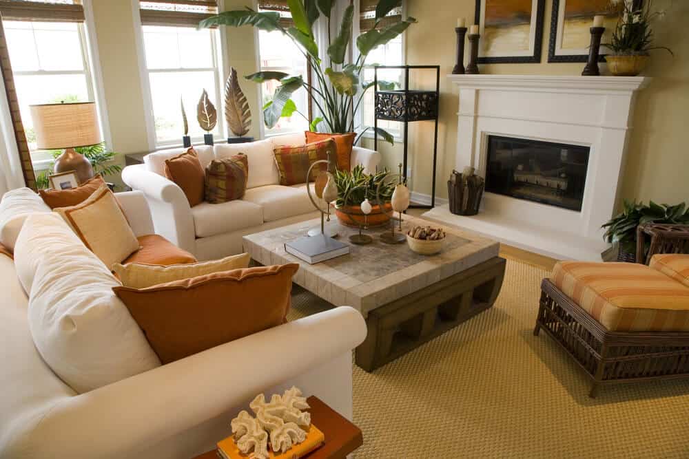 明亮多彩的客厅设计，米白色沙发装饰着橙色和棕色的枕头。一面墙的大窗户使空间充满了自然光线。