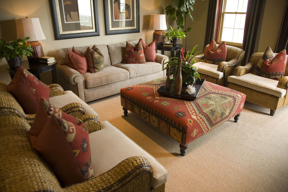 棕色和红色设计的毛绒客厅。里面有一张棕色沙发和四把扶手椅，围绕着一张有图案的软脚凳，它是一张大咖啡桌。棕色和红色图案的枕头。