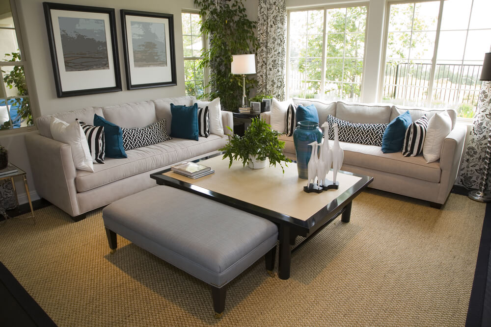 小屋风格的客厅，米白色的沙发装饰着白色和蓝色的枕头。茶几有深棕色的框架和浅棕色的顶部。茶几旁边是一张蓝色的长方形软脚凳。