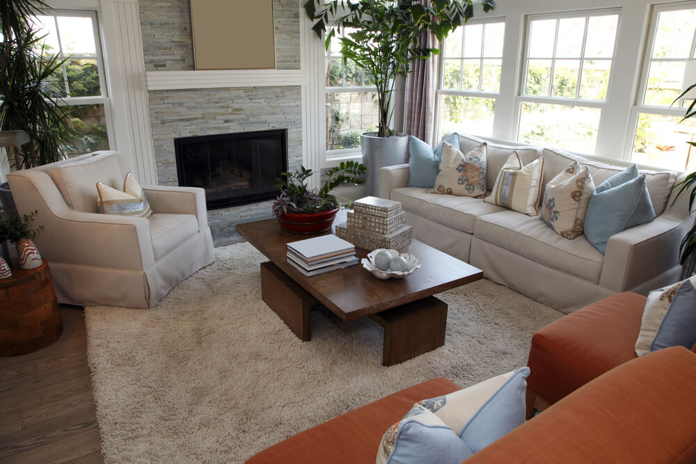 客厅空间有两把红褐色的椅子，一个米色沙发和一个米色扶手椅，围绕着一个长方形的现代木制咖啡桌。壁炉的框架是石墙和白色的冠饰。