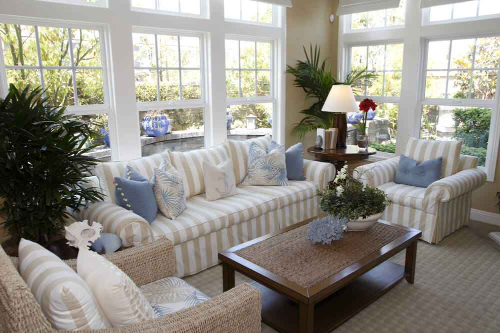 别墅风格的日光客厅，米色和白色条纹家具，一把扶手椅是柳条框架。客厅享受充足的自然光线从环绕的窗户。