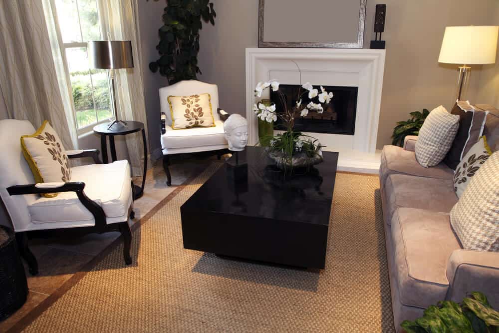 专业设计的客厅，白色壁炉，矩形深色街区风格的咖啡桌，两个白色扶手椅与深色木框和一个沙发对着窗户。