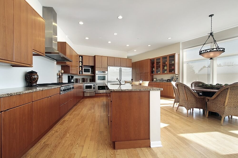均匀简约的厨房以光滑的深色木橱柜和架子为特色，放置在广阔的天然硬木地板上。