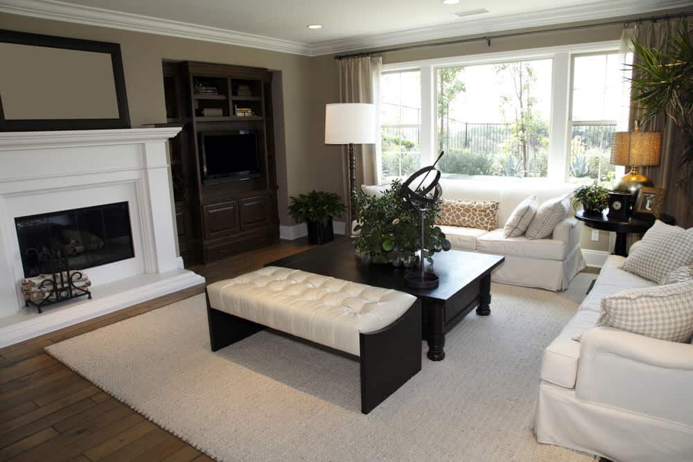 白色和深棕色的客厅设计。除了两张全白沙发外，还有一张深色木色的矮咖啡桌和深色木色和白色皮革的长凳。家具正对着一个巨大的白色壁炉。