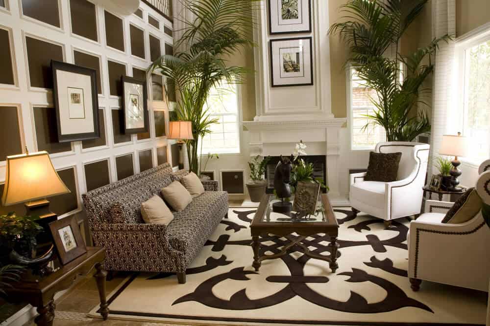 带高架天花板的客厅。两把白色扶手椅，一张长沙发，上面放着大印花地毯。房间的亮点是深棕色墙壁上的白色漆木框。