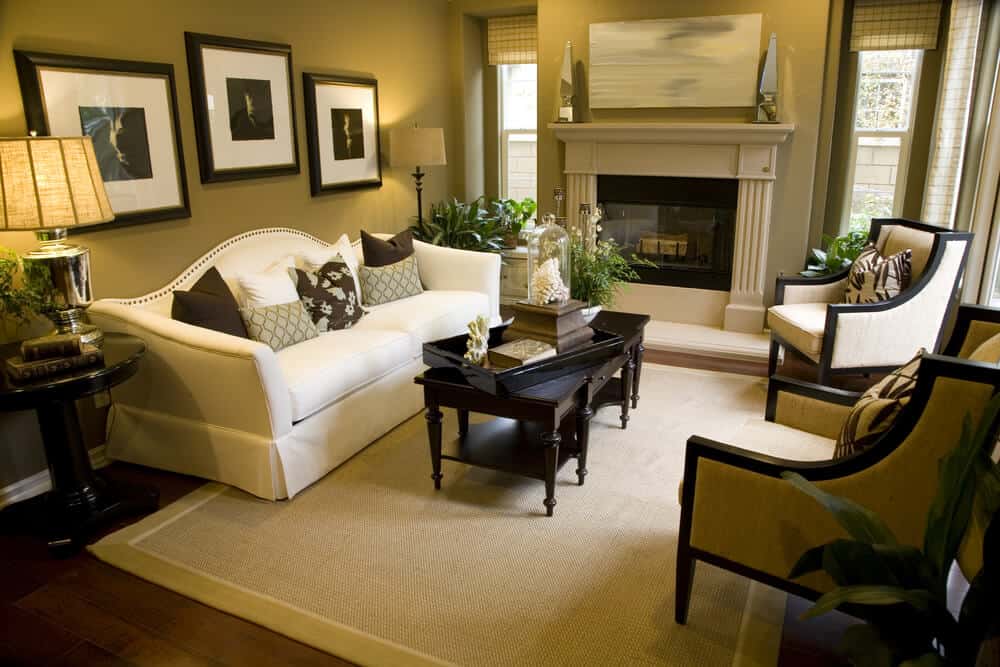 绿棕色的墙壁环绕着客厅，壁炉，白色沙发，两把扶手椅，深色木咖啡桌，硬木地板上有浅绿色边框的米黄色地毯。