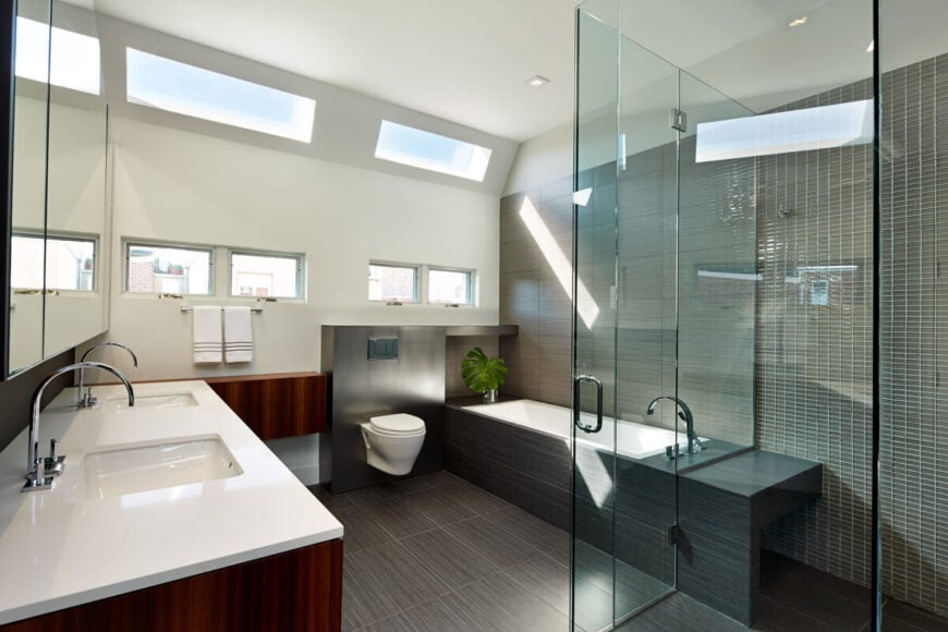 主浴室设有全玻璃淋浴，白色台面，红色木橱柜，深色木地板延伸到浴室周围。