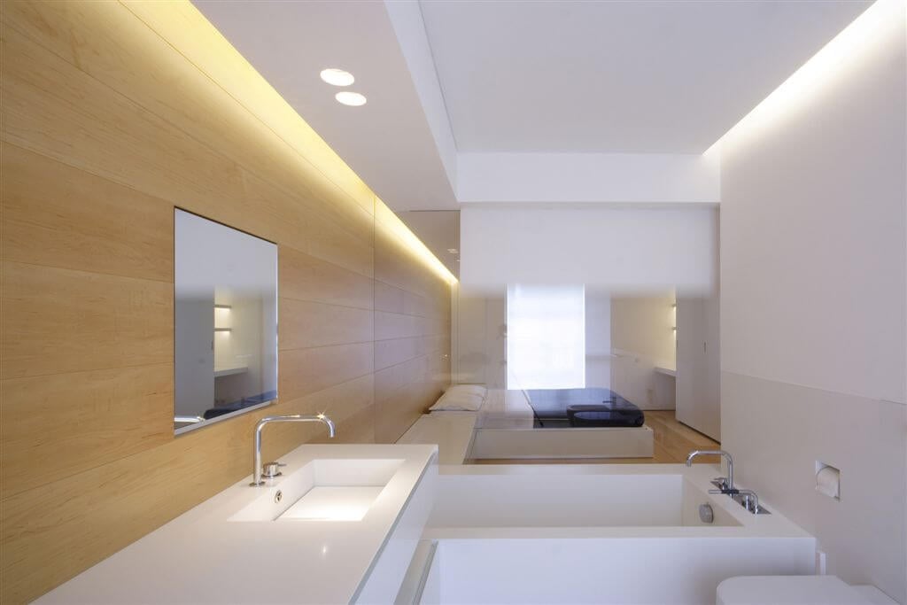 主浴室具有现代极简主义的尖锐角度和简单的白色和自然的木材色调。透明玻璃将卧室分隔开来。