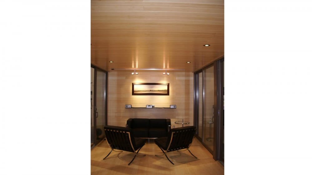 室内从地板到天花板，所有表面都有广泛的天然木材色调。黑色和金属家具与玻璃桌子构成了客厅空间。