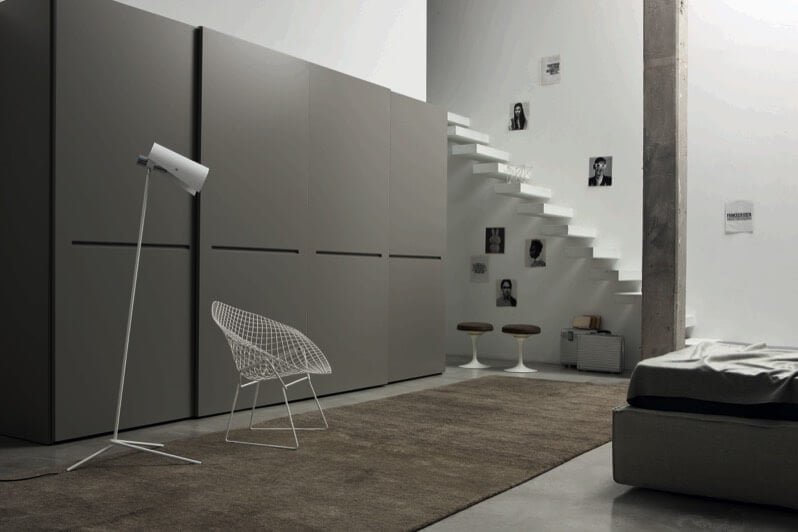 再次使用了大型的平齐开口面板，这次是灰色的，在一个以附墙的极简主义浮动楼梯和单一混凝土梁为特色的空间中。宽敞的棕色地毯和棕色凳子突出了房间后面的白色椅子和灯，和灰色的床架。