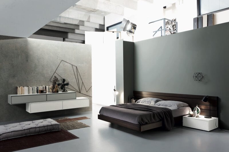 这个超现代的卧室设计以极简主义的灰色景观为特色，他们在其中放置了突出的元素:深色木床架和白色边桌的墙壁细节，分层地毯上的软垫地板座椅，以及白色和灰色的分层壁挂式搁架。
