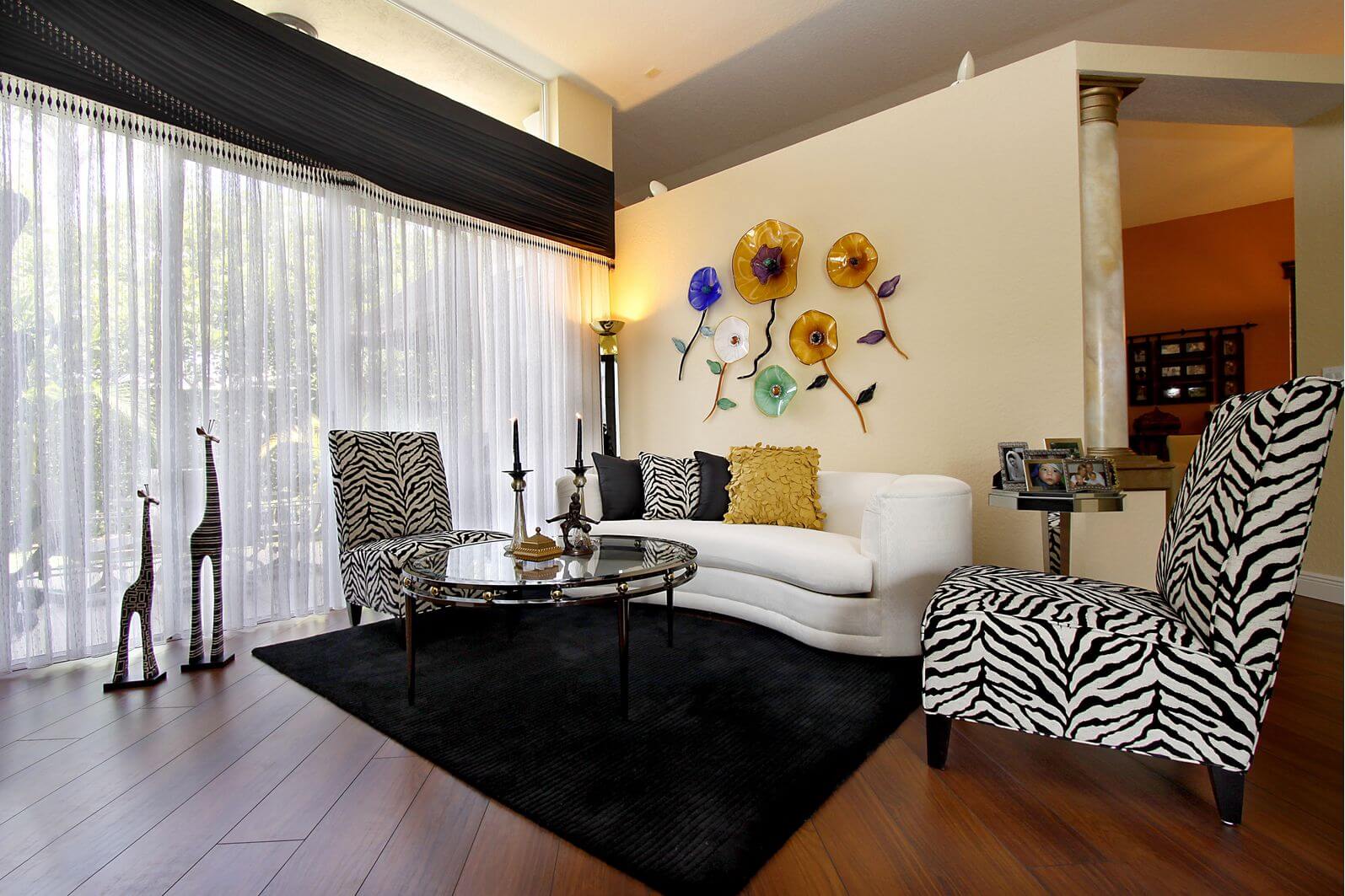 小客厅有2个斑马印花无扶手椅，一个白色小沙发，玻璃咖啡桌和木地板上的黑色地毯。这是斑马印花家具在小客厅设计中的一个很好的例子，看起来不错(即不过分)。