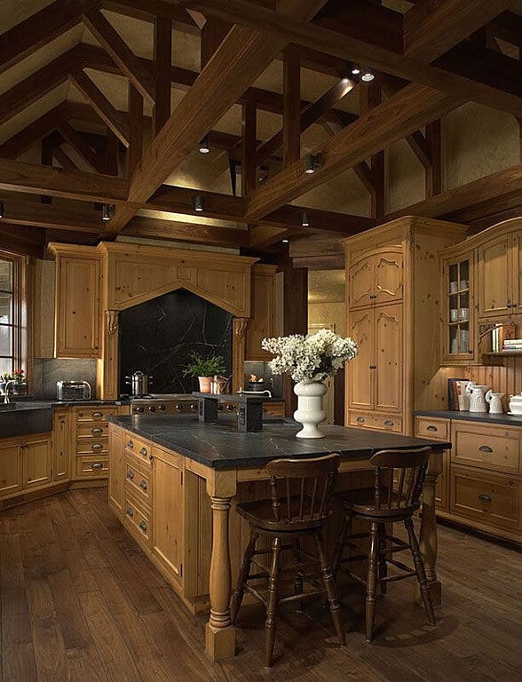 天然木橱柜的独特色调统一了这个厨房，夹在深色裸露的天花板横梁和配套的硬木地板之间。顶部是黑色大理石的岛控制着中心。