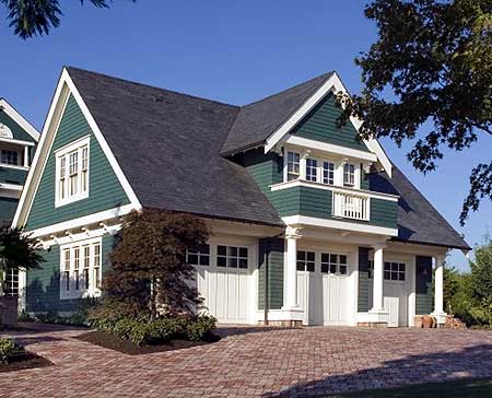 绿色和白色的三个隔间的马车房子的特点是白色车库门上的面板窗户，白色的柱子和上层阳台。
