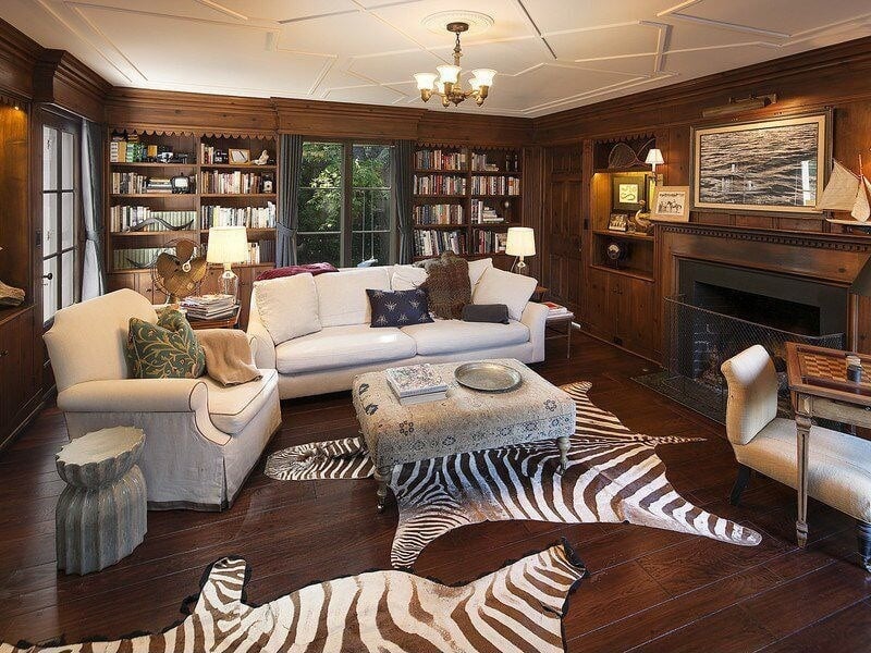 休闲的客厅设计，深色木地板，壁炉，白色家具，内置书架，木镶板和地板上的两只斑马皮