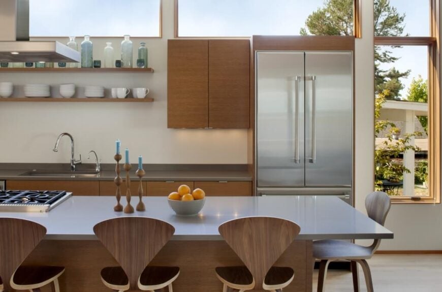 厨房区域的侧视图，突出灰色色调的台面和几乎匹配的铝制冰箱位于巨大的窗户下，完成了周围的开放视野。