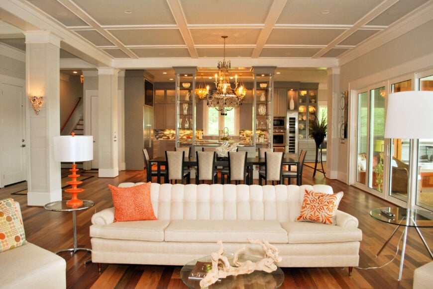 客厅设有白色沙发，橙色的色调，玻璃和金属桌子，背景是完整的用餐区。