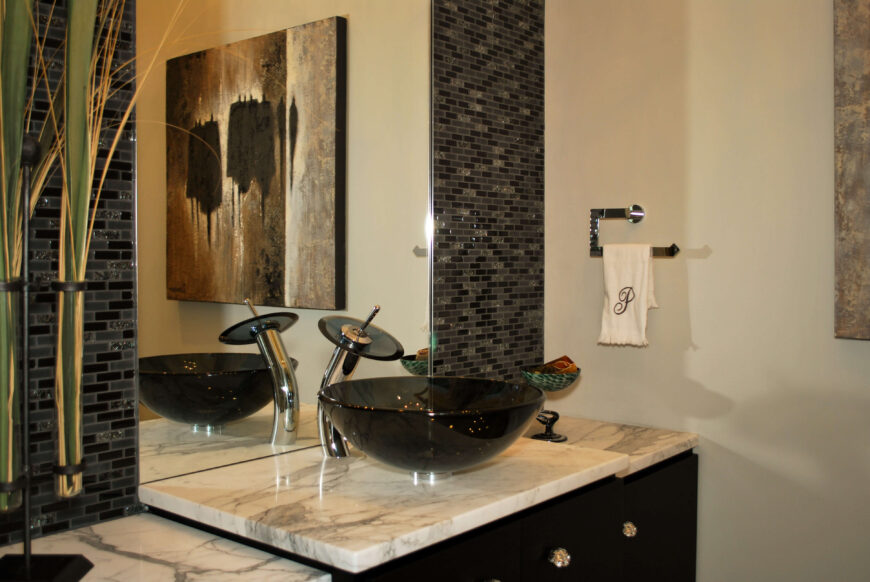 浴室设有浅大理石台面和黑色橱柜的容器水槽。瓷砖后挡板环绕镜子。