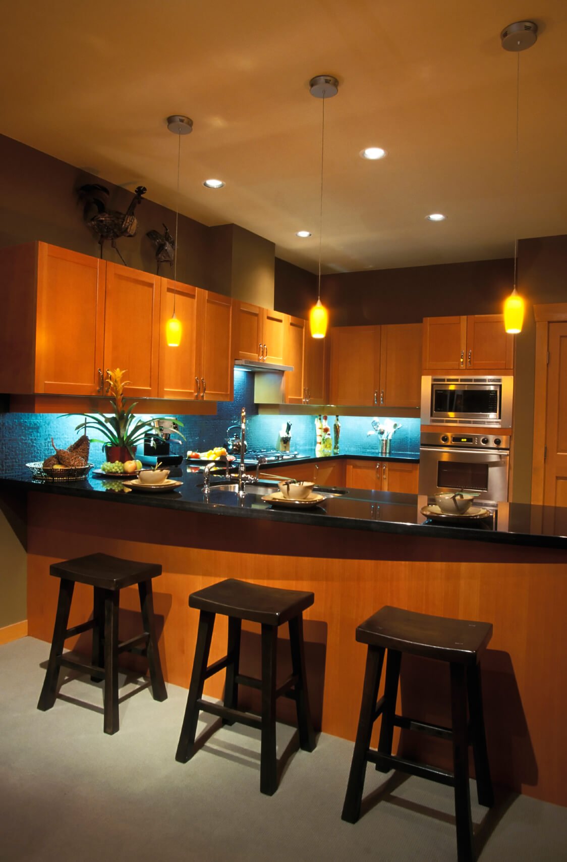现代风格的厨房采用温暖的自然木材色调，与光滑的黑色台面和蓝色瓷砖后挡板形成对比。