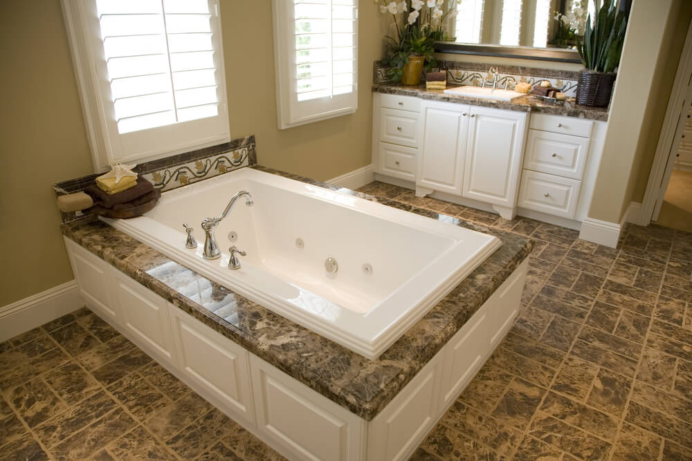 宽敞的棕色瓷砖地板与浴室中大理石顶部的浴缸外壳相匹配，整个浴室都有白色的木镶板。