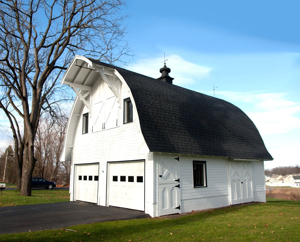 拱形屋顶谷仓风格的白色马车房设有两个隔间，车库门与3/4高的玻璃窗相匹配。
