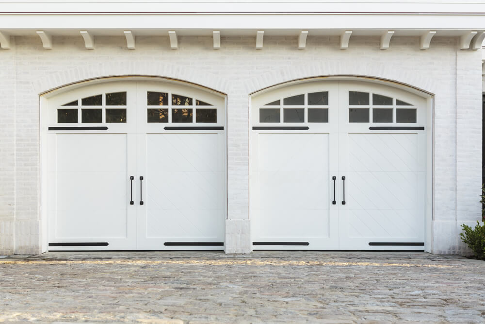 这座明亮的白色砖房设有两个车库，拱形砖框架的白色漆木马车风格的门。