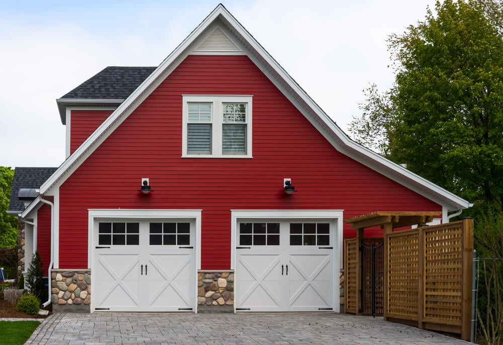 这个红色的侧向车库有两扇白色木门，带有上嵌板窗和悬挑灯。