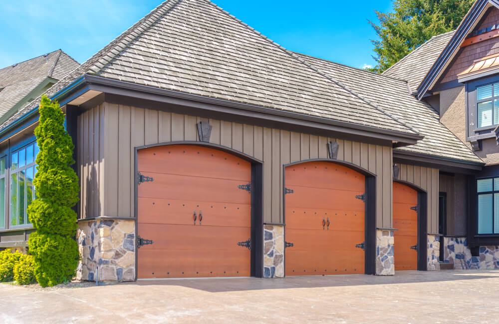面向三个车库的这一侧具有明亮的天然木质马车风格的门，框架为黑色，下层石材外墙。