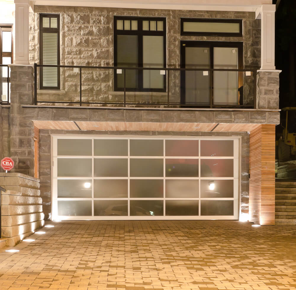 大型砖砌住宅设有较低的两个车库，带有单个大型烟熏玻璃门，框架为白色。