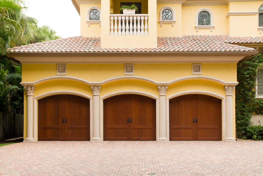 前延伸车库具有黄色立面，白色砖和柱子围绕着3个天然木马车风格的门。