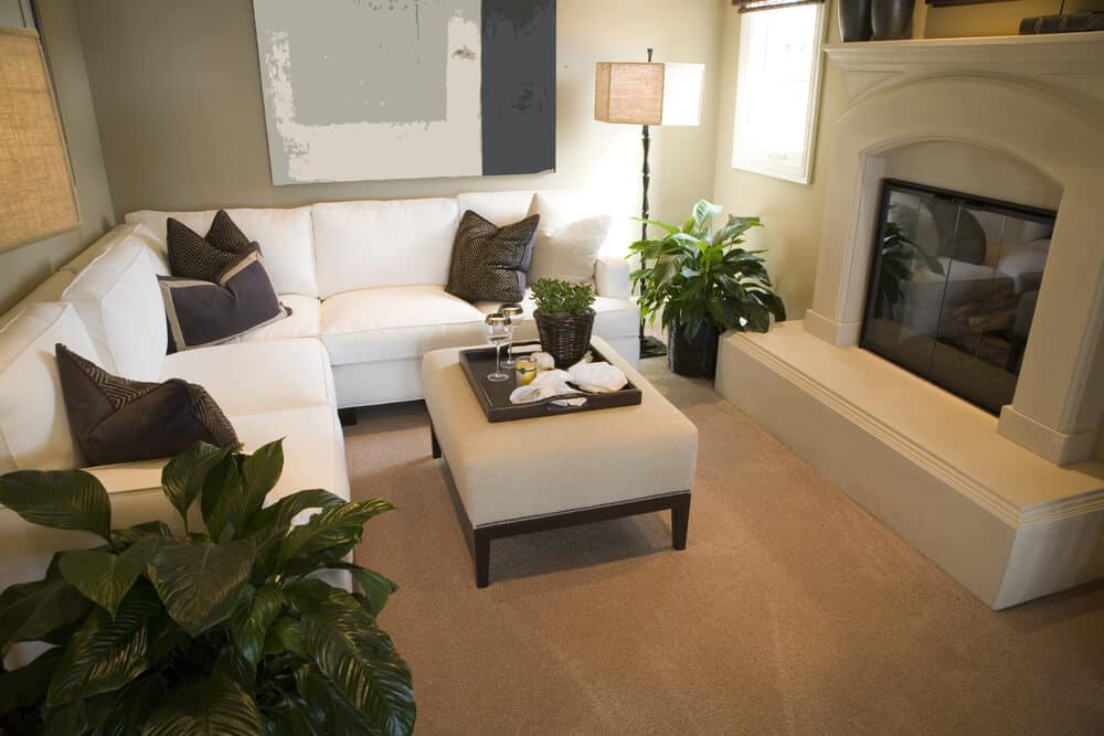 舒适的客厅，巨大的白色壁炉和白色l型组合沙发，深色木框架轻织物脚垫在中心，表面有深色木托盘桌。