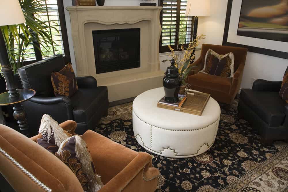 舒适的客厅，威严的石头壁炉，交替的橙色和黑色扶手椅，环绕指甲头装饰的白色皮革脚垫，便携式木质表面托盘。