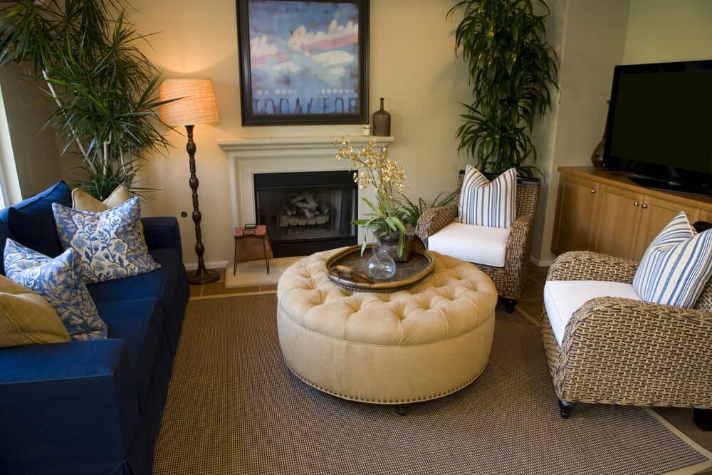 舒适的客厅中心圆形纽扣簇和钉子头修剪的脚凳之间的双柳条扶手椅和藏青色沙发。