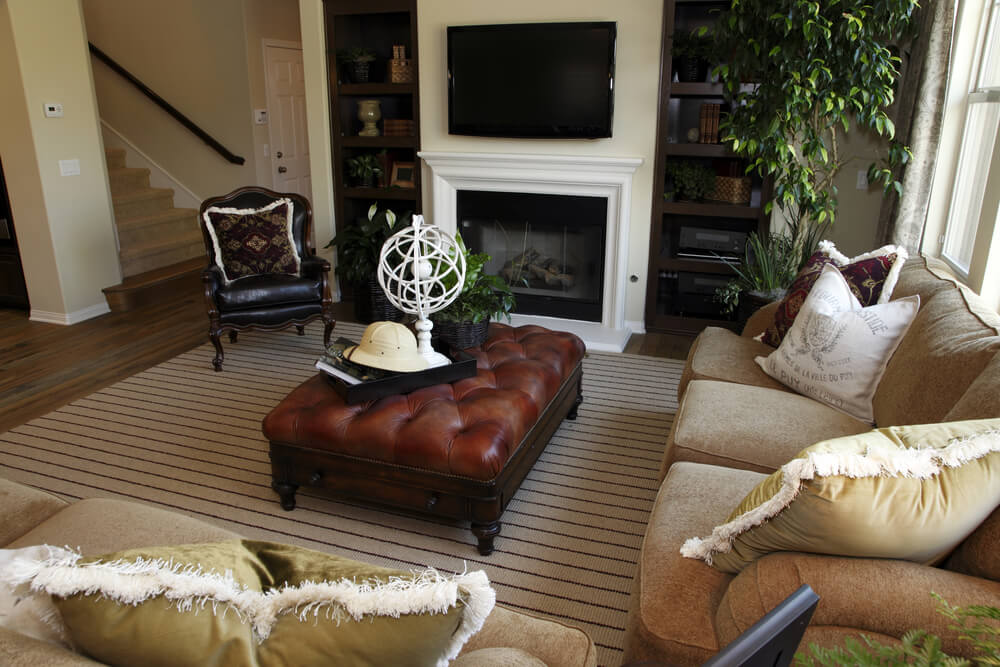 紧凑，优雅的客厅充斥着丰富的纹理，包括红色簇绒皮革和深色木脚凳在中心，在天然硬木地板上的条纹地毯。