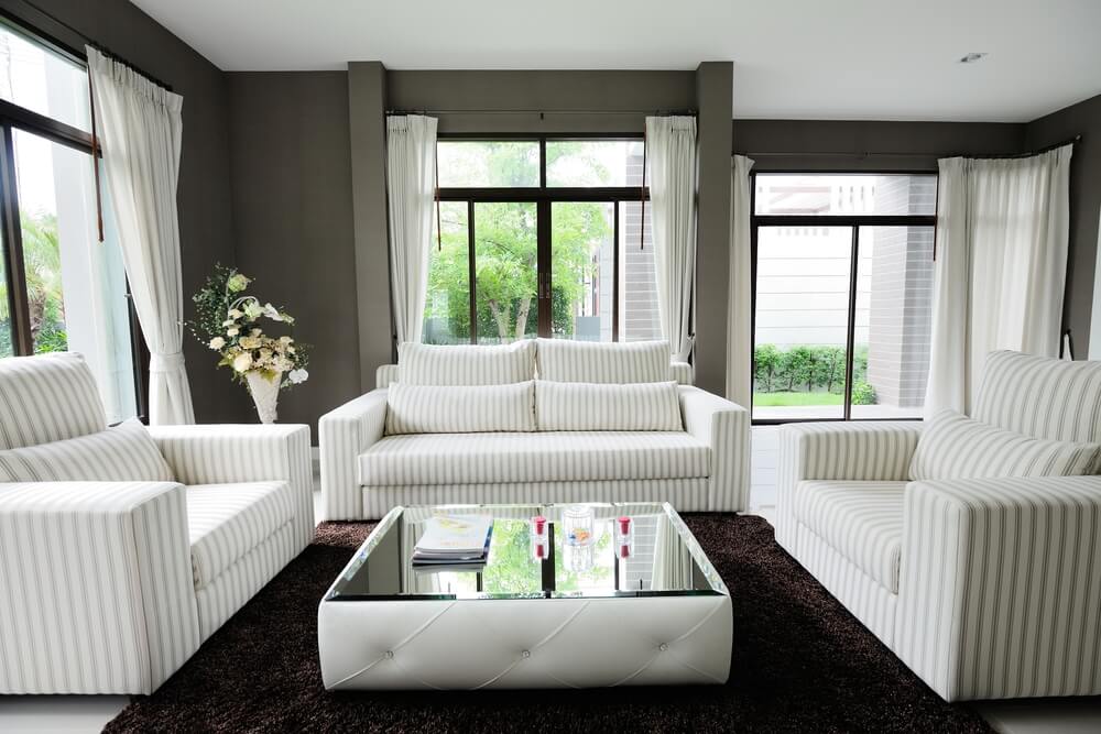 独特的低调方形白色簇绒软脚凳中心客厅，全镜面桌面表面在白色大理石地板上的深色地毯上。